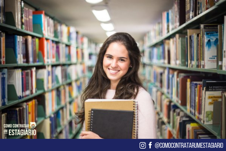 Estagiária com livros na mão, em uma biblioteca. Representando uma jovem que possui seguro para estagiários.