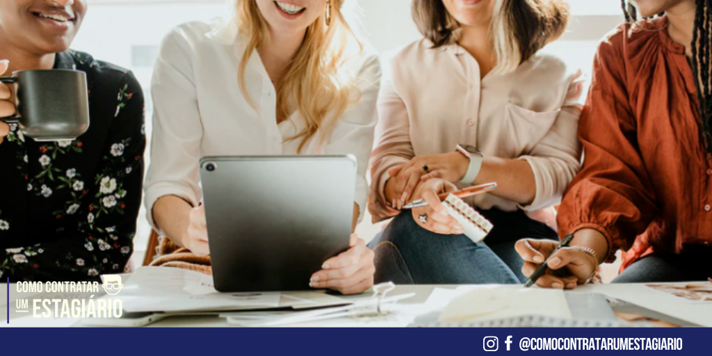 Quatro mulheres sorrindo no ambiente de trabalho representando o dia internacional das mulheres.